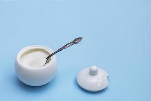 open white sugar bowl with a spoon inside and a lid next to it on a blue background with copy space photo