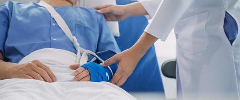 Injured patient showing doctor broken wrist and arm with bandage in hospital office or emergency room. Sprain, stress fracture or repetitive strain injury in hand. Nurse helping customer. First aid. photo