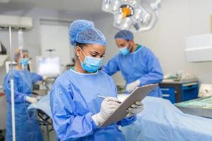 cirujano escritura en portapapeles en operación habitación, anestesiólogo escritura el actualizaciones foto