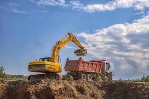 excavadora amarilla y camión volquete vacío trabajando en el sitio de construcción foto