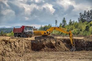 Yellow excavator and empty truck working at the construction site photo