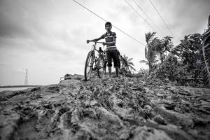 Bangladesh junio 27, 2015, un joven chico cruce a pesado lodoso la carretera a rasulpur, barisal distrito. foto