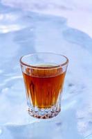 A glass of whiskey stands on a white background of ice. Orange drink in a glass. Top view from the side. For advertising alcoholic beverages. The background is blurry. Vertical. photo