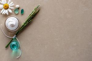 Flat view. Chamomile and a set of spikelets, white cream in a jar, blue liquid in the second jar and glass. Selective focus on the cream. Brown background blurred. Place for text. photo