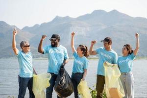 contento grupo de joven voluntarios Ayudar a mantener naturaleza limpiar y cosecha arriba el basura desde un arenoso costa. foto