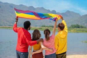 espalda vista. joven diversidad personas teniendo divertido participación lgbt arco iris bandera en el playa. partidarios de el lgbt comunidad foto
