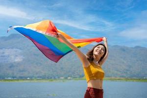 lesbiana mujer con gay orgullo, arco iris bandera en el playa en contra el cielo. joven mujer sonriente y levantamiento y ondulación el lgbt bandera en el aire en el playa. foto