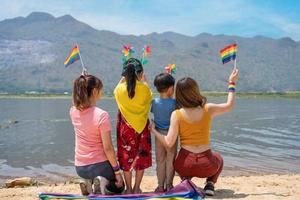 Back view. Young diversity people holding gay pride rainbow flag and colorful turbine on the beach. photo