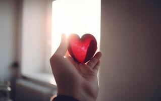 Hand showing red heart shape with sun rays in the background. . photo