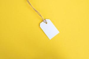 White tag with a thread on a yellow background. White price tag label mockup. Place to copy. photo