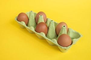 Brown chicken eggs in a tray with empty cells on a yellow background photo