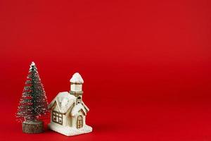 Navidad tarjeta. Navidad árbol y linda cabaña en un rojo antecedentes. foto