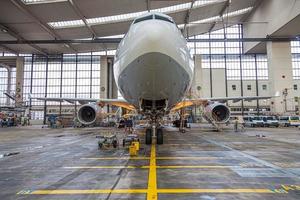 Frontal view to an white and grey colored airplane in maintenance hall photo