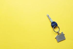 Key with a keychain in the form of a house on a bright yellow background. Place for inscriptions. photo