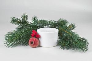 blanco crema tarro con Navidad árbol ramas y rojo Navidad cosas en un ligero antecedentes foto