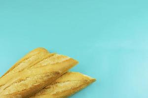 Tres francés baguettes en el izquierda inferior esquina en un ligero azul antecedentes foto