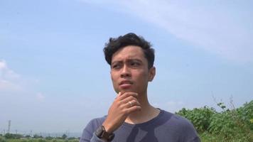 giovane uomo Indonesia pensare espressione su giorno leggero con natura cielo sfondo. il metraggio è adatto per uso per pubblicità e espressione soddisfare media. video