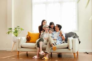 contento familia asiático familia, padres y niños contento sentado en el sofá en el casa. el familia relaja en el sofá en el vivo habitación. contento familia foto