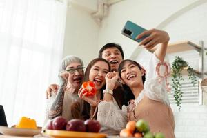 happy family Asian family taking selfies with smartphones together cooking food in the kitchen. spending time together cook together in the kitchen and dine together happily photo