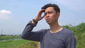 giovane uomo Indonesia fatica e depressione espressione su giorno leggero con natura cielo sfondo. il metraggio è adatto per uso per pubblicità e espressione soddisfare media. video