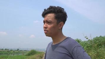 giovane uomo Indonesia fatica e depressione espressione su giorno leggero con natura cielo sfondo. il metraggio è adatto per uso per pubblicità e espressione soddisfare media. video