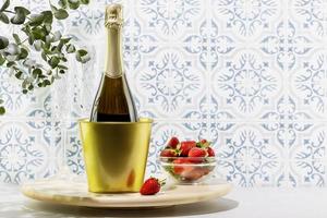 Bottle of champagne and fresh strawberries in a glass bowl on wooden podium photo