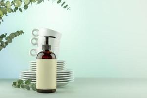 Bottle with dish detergent with clean plates and cups with eucalyptus branches photo