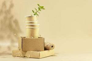 Cardboard boxes, disposable cups with green shoot on beige background photo