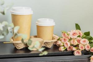 Two disposable cups of coffee and bouquet of roses on wooden table photo