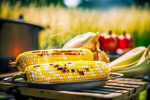 Delicious grilled corn cobs with appetizing crust, rosmarin on plate near barbecue grill on blurred countryside view background. Vegan healthy food. Vegetarian barbeque. photo