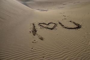 heart symbol of love arranged from gray stone on golden sand on a golden dune photo