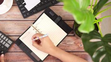 Top view of woman hand using calculator and writing on notepad on office desk video