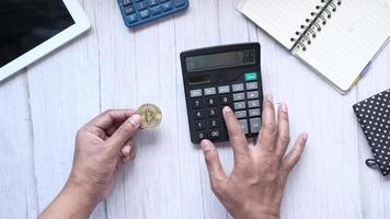 Holding golden bitcoins and typing on calculator video