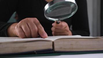 Close-up of a woman looking through a magnifying glass at a textbook. Magnifying glass in hand and open book on table. Education and research concept. video