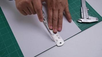 Nahansicht Hände von weiblich Schneiden Papier mit Nützlichkeit Messer Cutter. weiblich Hand mit Messer Schneiden Papier durch Lineal auf Schneiden Matte. video