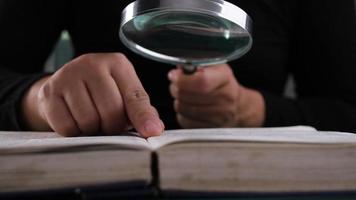 Close-up of a woman looking through a magnifying glass at a textbook. Magnifying glass in hand and open book on table. Education and research concept. video
