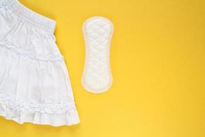 White skirt and woman sanitary pad on yellow background. Female menstruation cycle period. Hygiene concept. Linen and health protection idea. Copy space photo