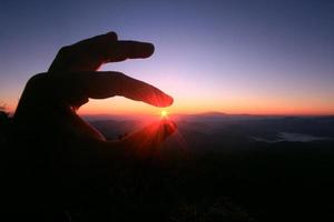 Woman fingers pick beautiful sun in natural twilight of sunset on the mountain photo