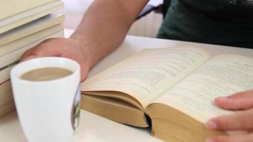 leerling lezing boek en drinken koffie, leerling drinken koffie terwijl aan het studeren van oud boeken, selectief focus video