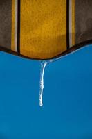 an icicle against a blue sky hanging from a yellow awning photo