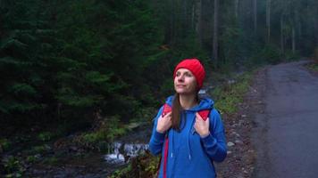 femme voyageur avec une sac à dos des promenades sur le route dans le montagnes le long de le rivière et admire le alentours paysage video