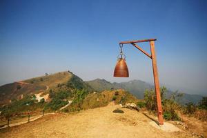 Old rusty bell with Dry grassland and wild with blue sky on the valley mountain at Doi Pha Tang hill in Thailand photo