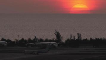 PHUKET, THAILAND FEBRUARY 11, 2023 - Passenger aircraft on airport taxiway against the backdrop picturesque sunset. Boeing 737 of NOK Air taxiing. Sea and red sunset background. Travel concept video
