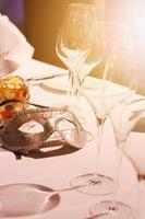 Silver mask, wine glass and  yellow candle decoration on white tablecloth with golden light in Christmas  and new year party. photo