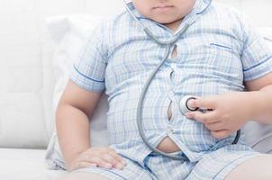 Obese fat boy check stomach by stethoscope photo