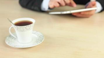 Geschäftsmann Trinken ein Tasse von Tee während Arbeiten auf Tablette, mit Tablette zum Büro funktioniert, selektiv Fokus video