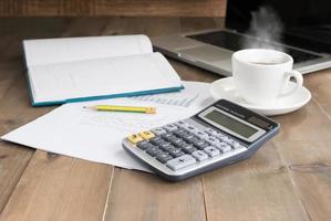 calculadora y caliente café con computadora cuaderno en madera foto