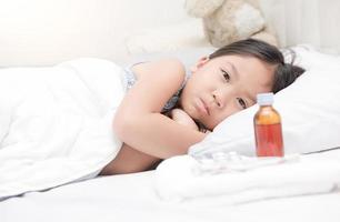 enfermo niña acostado en cama y medicina jarabe foto