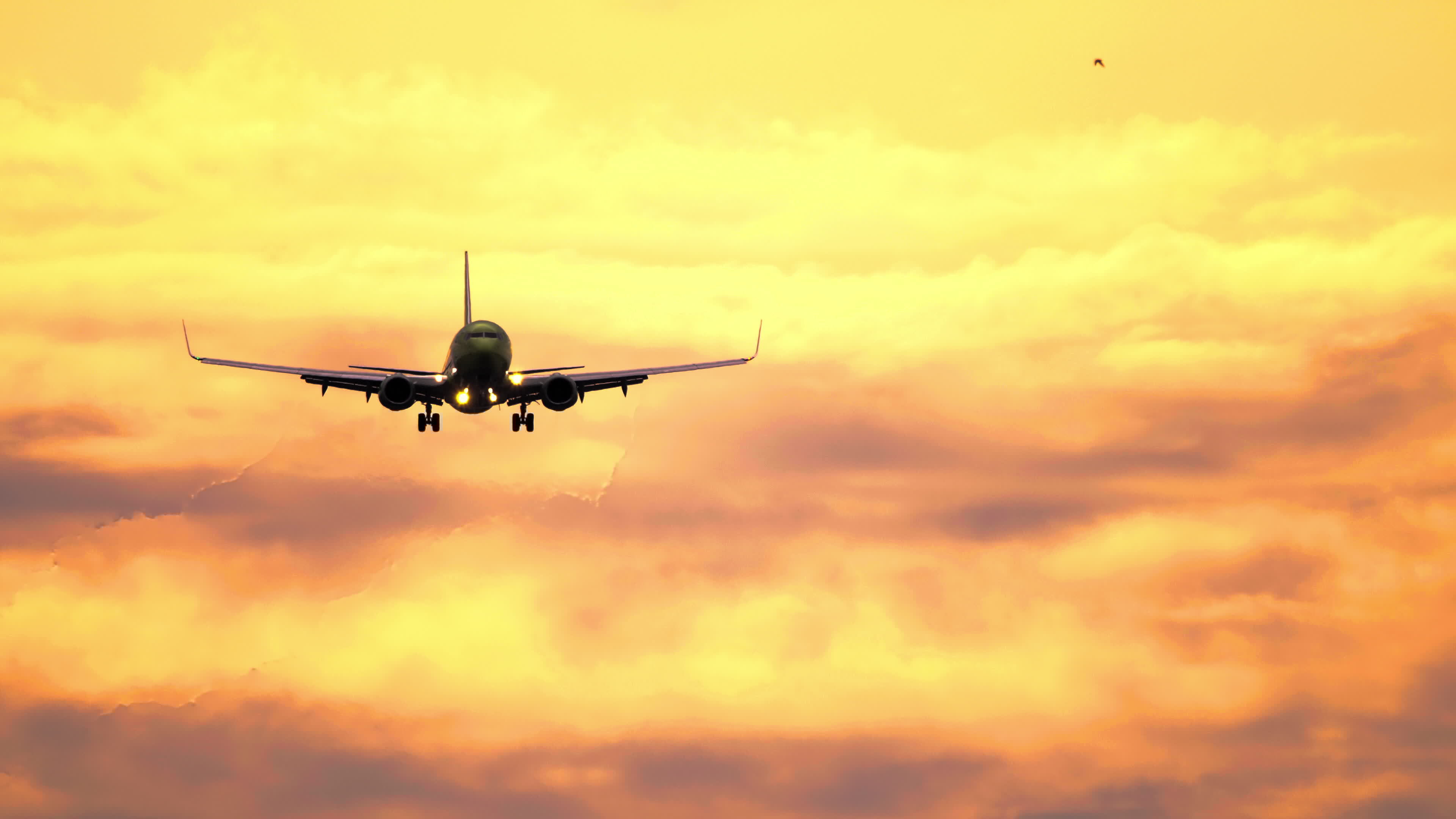 Silhouette of aircraft flying in orange sunset sky with clouds illuminated by setting sun