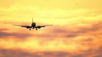 silhouette di aereo volante nel arancia tramonto cielo con nuvole illuminato di ambientazione sole. bellissima Cloudscape con aereo. volo di aereo con lampeggiante luci a tramonto video